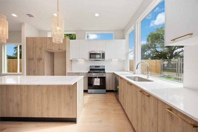 kitchen with a sink, light wood-type flooring, visible vents, modern cabinets, and appliances with stainless steel finishes