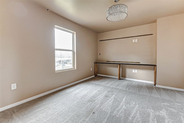 carpeted empty room featuring baseboards and an inviting chandelier