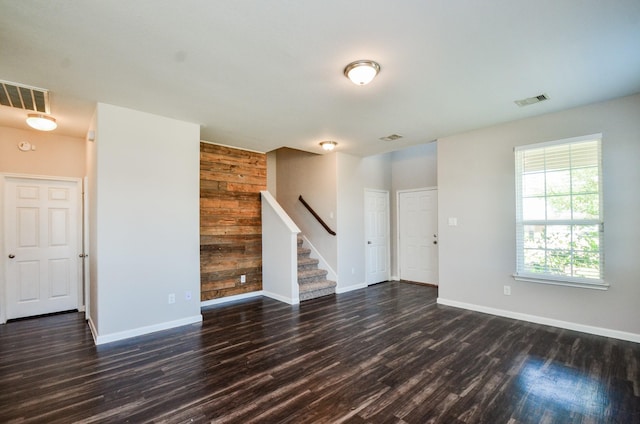 empty room featuring baseboards, visible vents, dark wood-style floors, and stairs