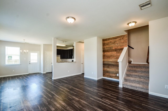 unfurnished living room featuring stairway, an inviting chandelier, baseboards, dark wood-type flooring, and visible vents
