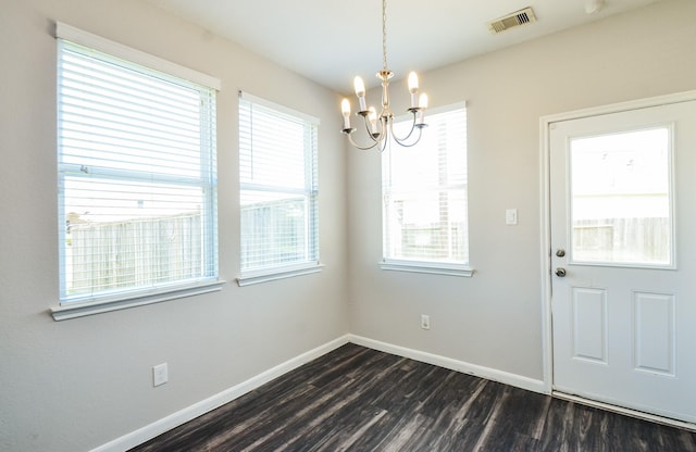 unfurnished dining area featuring dark wood-type flooring, visible vents, baseboards, and an inviting chandelier