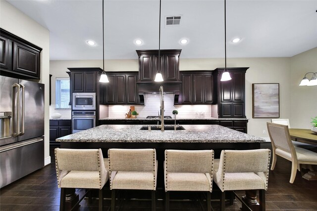 182 River Wilde Dr, Montgomery, TX 77316 - kitchen featuring appliances with stainless steel finishes, a breakfast bar area, decorative backsplash, light stone counters, and a center island with sink