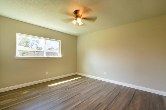 empty room featuring baseboards, a ceiling fan, and dark wood-style floors