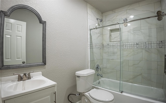 bathroom featuring toilet, a textured wall, vanity, and bath / shower combo with glass door