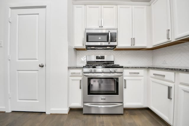 kitchen with stainless steel appliances, dark stone counters, dark wood finished floors, white cabinetry, and decorative backsplash
