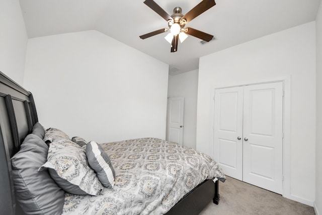 bedroom with vaulted ceiling, a closet, light colored carpet, and a ceiling fan