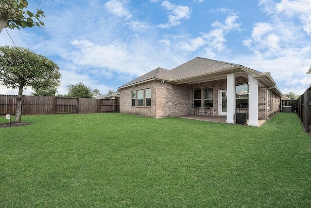back of property with a fenced backyard, a yard, roof with shingles, a patio, and brick siding