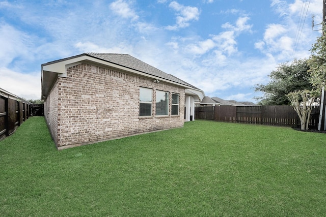 rear view of house with a fenced backyard, brick siding, and a yard