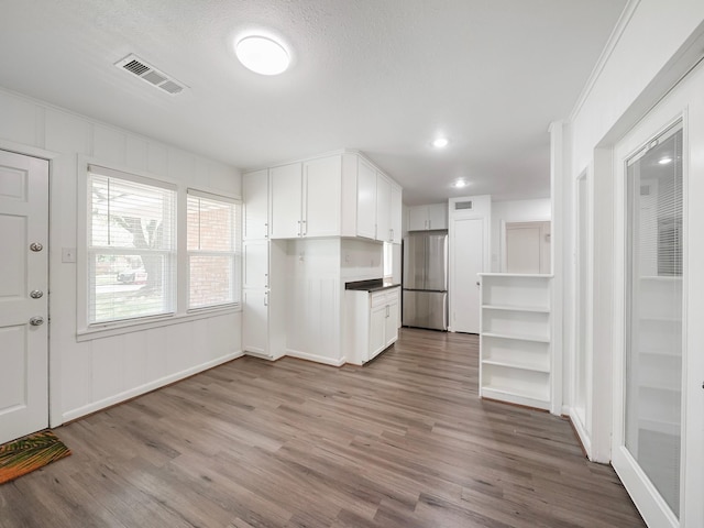 9710 Bassoon Dr, Houston, TX 77025 - kitchen featuring white cabinets, wood finished floors, visible vents, freestanding refrigerator, and baseboards