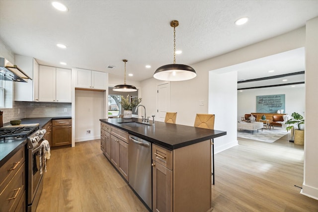 kitchen featuring white cabinets, stainless steel appliances, light wood-style flooring, a sink, and dark countertops