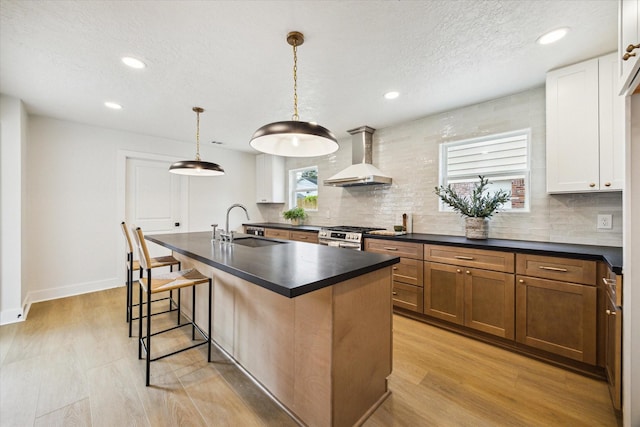 kitchen featuring a kitchen breakfast bar, a sink, dark countertops, decorative backsplash, and wall chimney range hood