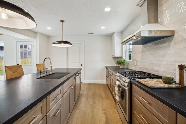 kitchen featuring wall chimney exhaust hood, stainless steel appliances, light wood finished floors, a sink, and dark countertops