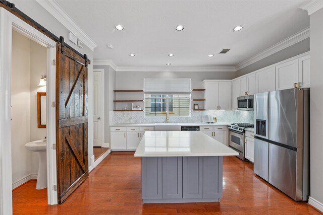 kitchen featuring a barn door, open shelves, light countertops, a sink, and appliances with stainless steel finishes