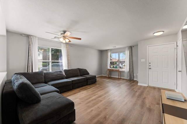 living area featuring light wood-style flooring, a textured ceiling, a ceiling fan, and baseboards