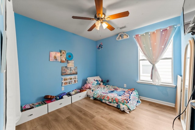 bedroom with baseboards, a ceiling fan, wood finished floors, and visible vents