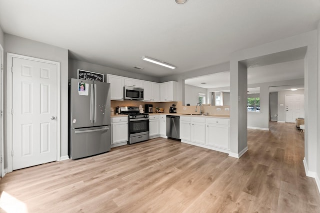 kitchen with light wood finished floors, a sink, white cabinetry, light countertops, and appliances with stainless steel finishes