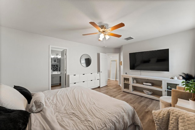 bedroom featuring a ceiling fan, wood finished floors, visible vents, and ensuite bathroom