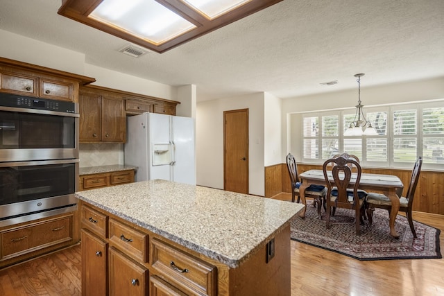 13018 Lentando Ln, Cypress, TX 77429 - kitchen featuring white refrigerator with ice dispenser, double oven, dark wood finished floors, brown cabinetry, and a wainscoted wall