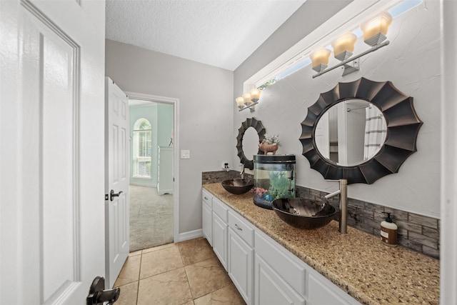 bathroom with a textured ceiling, tile patterned flooring, double vanity, and a sink