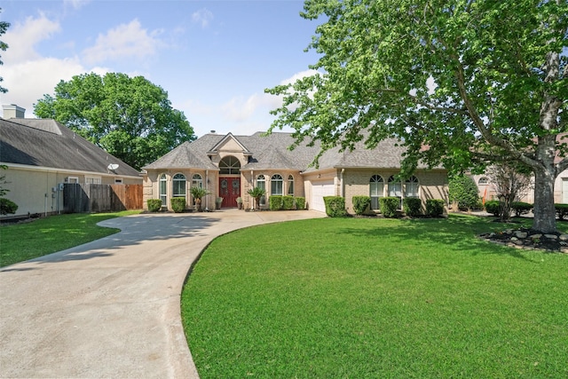french provincial home featuring an attached garage, a front lawn, brick siding, and driveway
