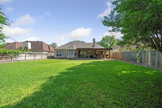 back of property featuring a fenced backyard, a patio area, a chimney, and a lawn