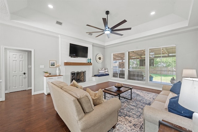 living room with wood finished floors, visible vents, ceiling fan, a large fireplace, and a raised ceiling