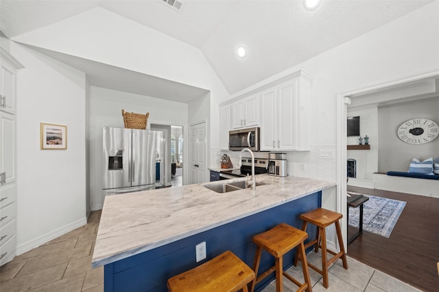 kitchen featuring light tile patterned flooring, a sink, white cabinetry, vaulted ceiling, and stainless steel appliances