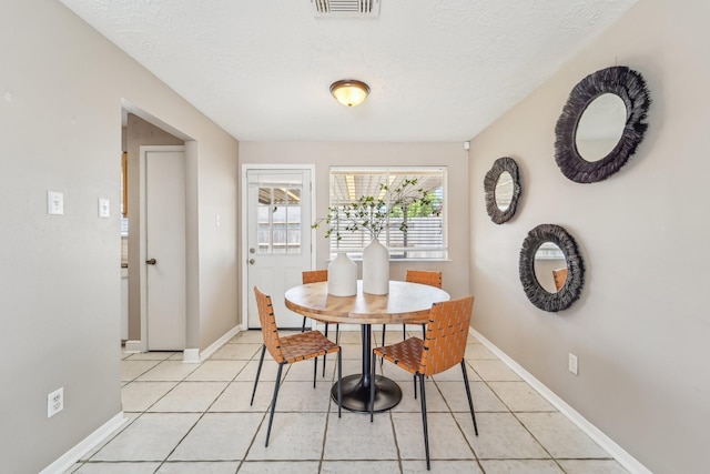dining space featuring baseboards, a textured ceiling, visible vents, and light tile patterned floors