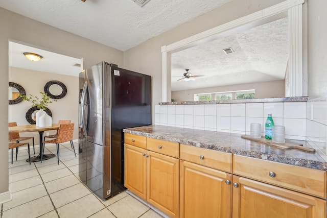 kitchen featuring a textured ceiling, light tile patterned flooring, freestanding refrigerator, decorative backsplash, and a ceiling fan