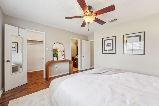 bedroom with wood finished floors, visible vents, a walk in closet, a closet, and baseboards