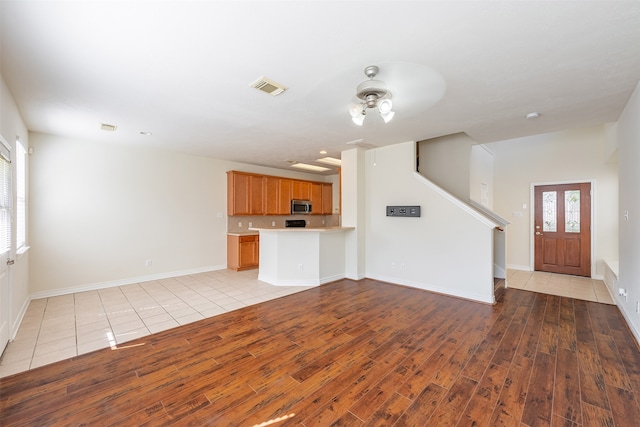 unfurnished living room featuring visible vents, a ceiling fan, light wood-style flooring, and baseboards