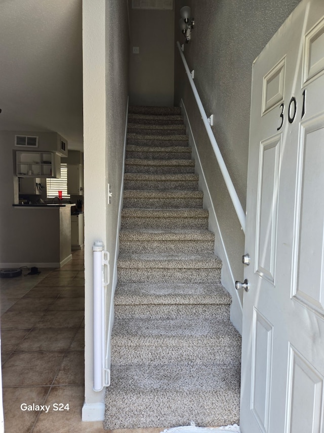 staircase with visible vents, a textured wall, and tile patterned flooring