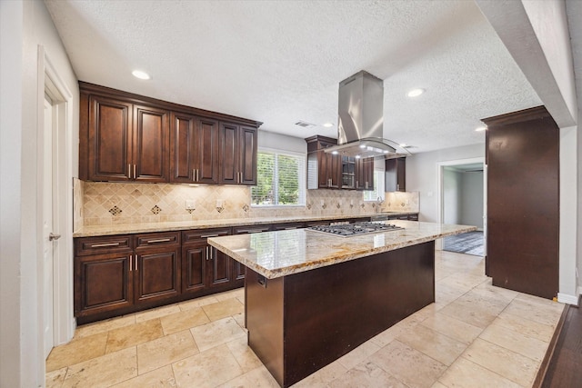 kitchen featuring stainless steel gas cooktop, island exhaust hood, tasteful backsplash, a textured ceiling, and dark brown cabinets