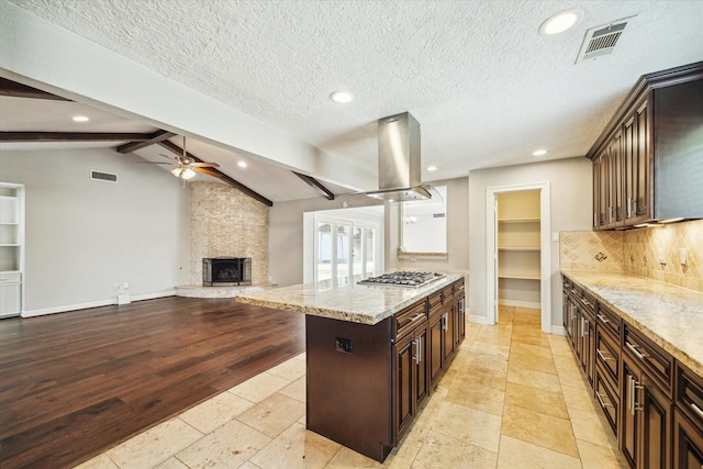 kitchen with island range hood, ceiling fan, stainless steel gas stovetop, tasteful backsplash, and a fireplace