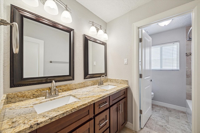 full bath with a textured ceiling, baseboards, toilet, double vanity, and a tub