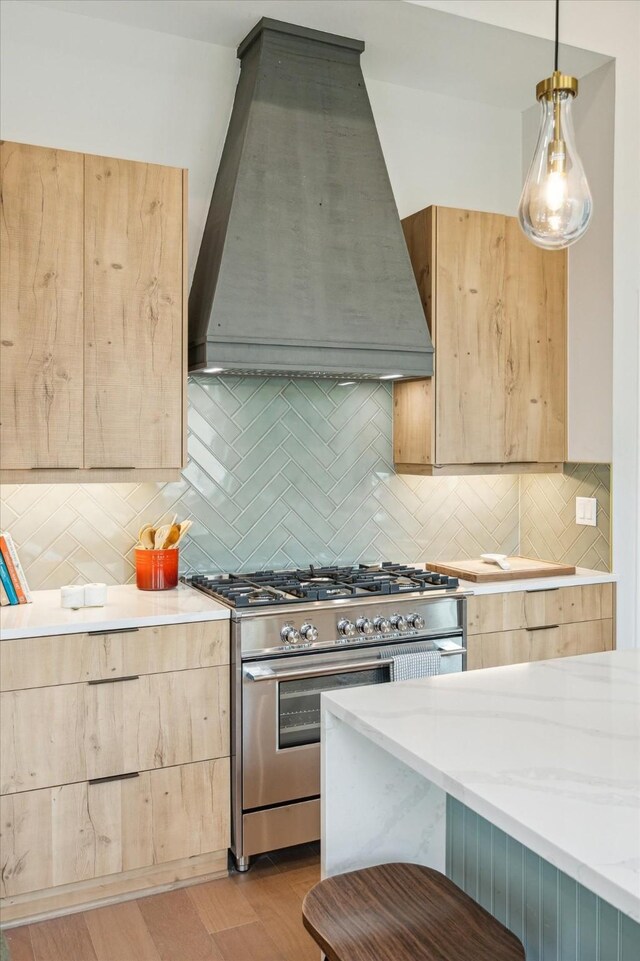 kitchen featuring stainless steel range, light brown cabinetry, custom range hood, and tasteful backsplash