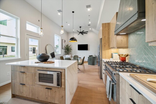 kitchen with modern cabinets, custom exhaust hood, light brown cabinetry, and appliances with stainless steel finishes