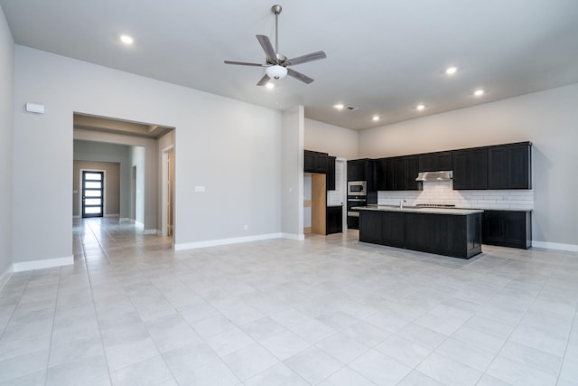 kitchen with tasteful backsplash, dark cabinetry, a ceiling fan, light countertops, and under cabinet range hood