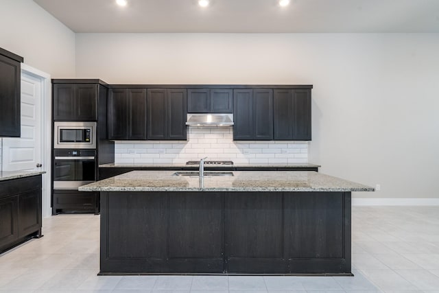kitchen featuring tasteful backsplash, a sink, appliances with stainless steel finishes, under cabinet range hood, and light stone countertops