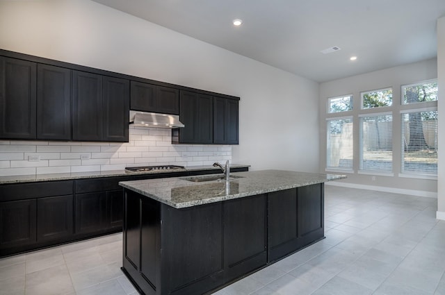 kitchen featuring light stone counters, a sink, stainless steel gas cooktop, under cabinet range hood, and visible vents