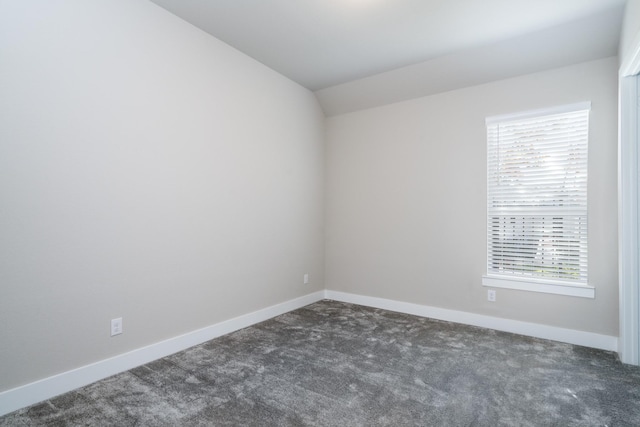 spare room with vaulted ceiling, dark colored carpet, and baseboards