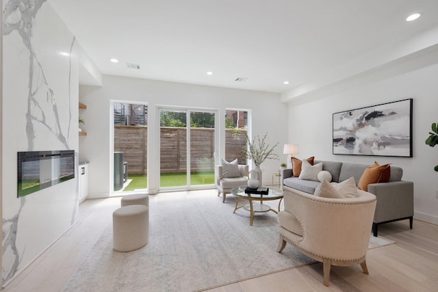 living area featuring a premium fireplace, recessed lighting, visible vents, and light wood-type flooring