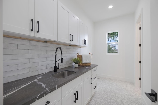 kitchen featuring dark stone counters, tasteful backsplash, a sink, baseboards, and white cabinetry