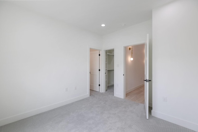 unfurnished bedroom featuring light colored carpet, baseboards, a walk in closet, and recessed lighting