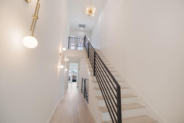 stairway with baseboards, wood finished floors, a towering ceiling, and visible vents