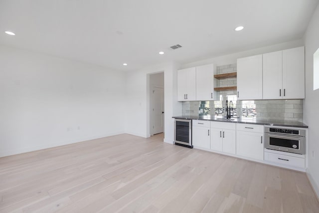kitchen featuring wine cooler, open shelves, decorative backsplash, stainless steel oven, and white cabinetry
