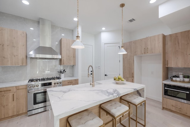 kitchen with wall chimney exhaust hood, modern cabinets, light brown cabinetry, and appliances with stainless steel finishes