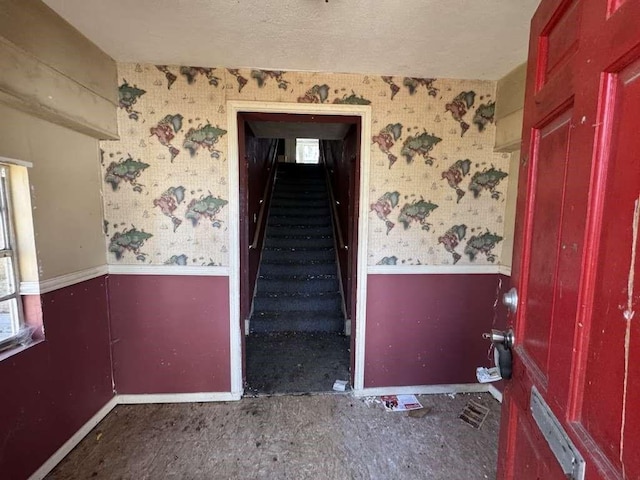 stairway with wallpapered walls, a wainscoted wall, and a textured ceiling