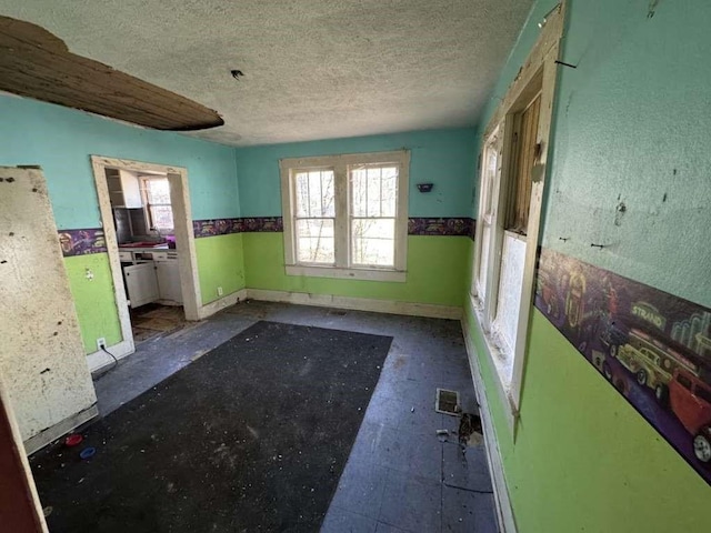 empty room featuring a textured ceiling, a wealth of natural light, baseboards, and visible vents