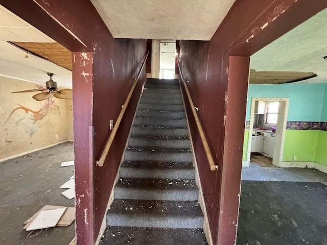 stairs with a ceiling fan and baseboards